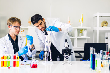 Professional two scientist man research and working doing a chemical experiment while making analyzing and mixing liquid in test tube.Young science man dropping sample chemical on glass at laboratory