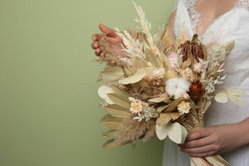 Bride holding beautiful dried flower bouquet on green background, closeup. Space for text