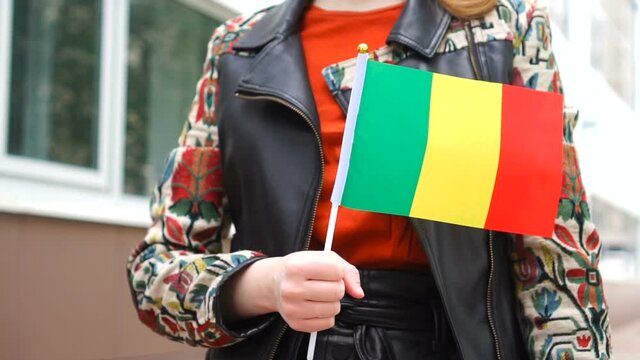 Unrecognizable woman holding Malian flag. Girl walking down street with national flag of Mali