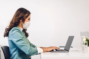 Young asian business woman using laptop computer working and planning meeting in quarantine for coronavirus wearing protective mask with social distancing while sitting on office desk