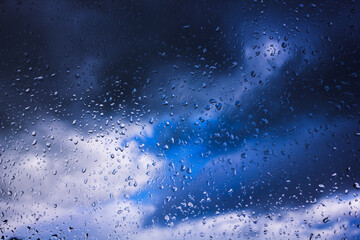 Raindrops on a window with storm clouds behind it.