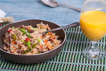 Spicy Mexican vegetarian dish - cooked rice with chili and red beans in a plate with green onions on the table with a glass of citrus juice