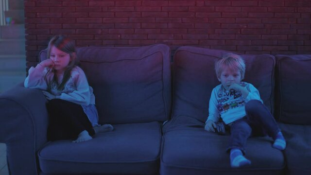 two children sitting on the couch watching tv