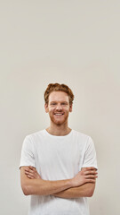  Young redhead man stands with arms folded and looks straight in camera