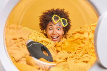 Positive young Afro American woman does laundering at home smliles broadly has fun wears snorkeling...