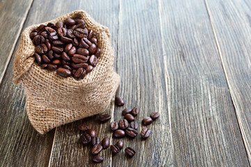 Roasted coffee beans in a burlap sack on a wooden background. Copy space. Coffee export concept