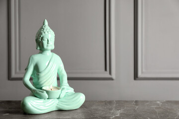 Buddha statue with burning candle on grey table. Space for text