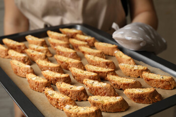 Woman holding baking tray with tasty cantucci indoors, closeup. Traditional Italian almond biscuits