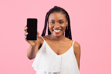 Positive African American lady holding cellphone with mockup for design, smiling at camera over pink studio background