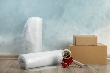 Bubble wrap rolls, tape dispenser and cardboard boxes on floor near light blue wall
