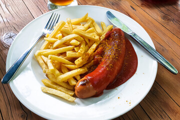 White plate with curry sausage and French fries on a wooden table in a Bavarian beer garden