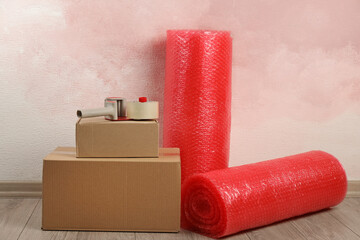 Red bubble wrap rolls, tape dispenser and cardboard boxes on floor near pink wall