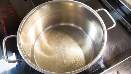 Stainless steel pot filled with olive oil on the hob of a modern cooker