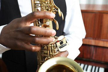 African-American man playing saxophone indoors, closeup. Talented musician