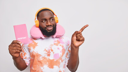 Dark skinned man traveler listens music via headphones dressed in washed out t shirt uses travel...