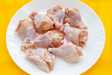 Fresh raw chicken wings (wingstick) in white plate on yellow background.
