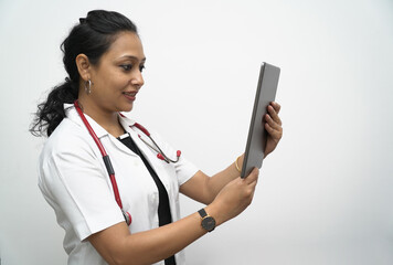 A south Indian female doctor in 30s holding tablet in white coat and red stethoscope in white...