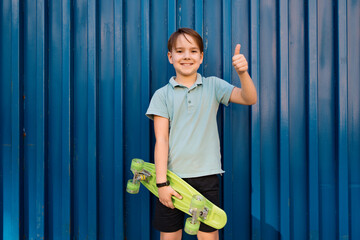 Portrait Young cool smiling BOY in blue polo posing with PENNY BOARD in the hands on a blue...