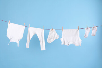 Clean child's clothes hanging on laundry line against light blue background