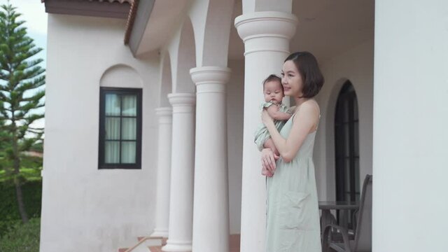 portrait of asian woman mother holding baby infant on balcony terrace at luxury home looking away the morning view. happy smile 30's female parent and 6 months baby at home near garden daytime. - Powered by Adobe