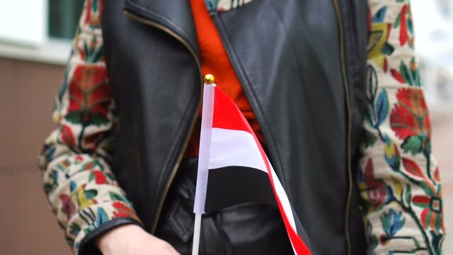 Unrecognizable woman holding Yemeni flag. Girl walking down street with national flag of Yemen