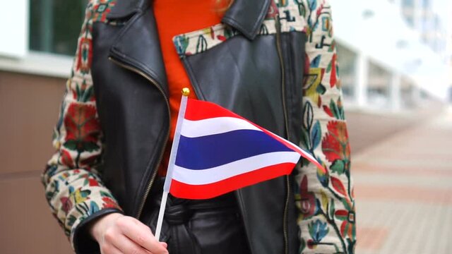 Unrecognizable woman holding Thai flag. Girl walking down street with national flag of Thailand