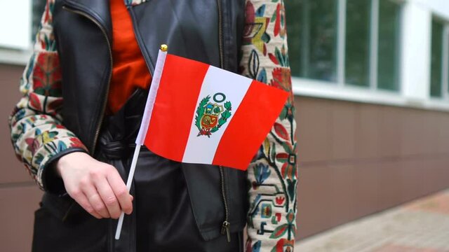 Unrecognizable woman holding Peruvian flag. Girl walking down street with national flag of Peru