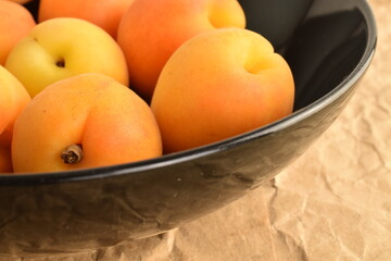 Several ripe organic yellow apricots in a black plate, close-up, on craft paper.