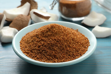 Natural coconut sugar in ceramic bowl on blue wooden table, closeup