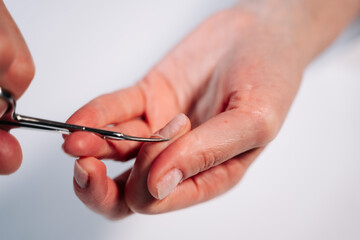 Home manicure. In the photo, a woman cuts off a raised cuticle with manicure scissors.