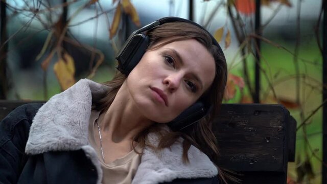 portrait of a sad woman wearing headphones. she leaned her head against the back of the bench