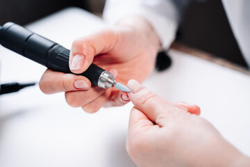 Fototapeta premium Home manicure. In the photo, a woman removes the top layer of the nail plate using a nail cutter.