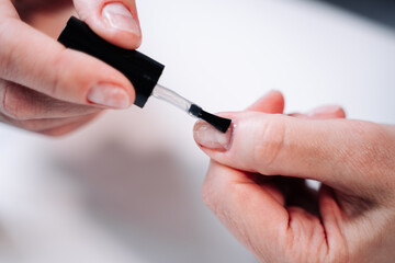 Home manicure. In the photo, a woman applies a beige gel polish (coating, base) with a brush for further drying under a manicure lamp.