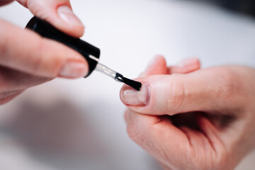 Home manicure. In the photo, a woman applies a beige gel polish (coating, base) with a brush for further drying under a manicure lamp.