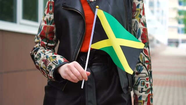 Unrecognizable woman holding Jamaican flag. Girl walking down street with national flag of Jamaica