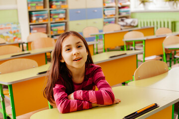 The joyful schoolgirl is sitting at a desk in the classroom