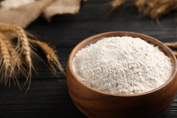 Bowl of flour on black wooden table, closeup. Space for text