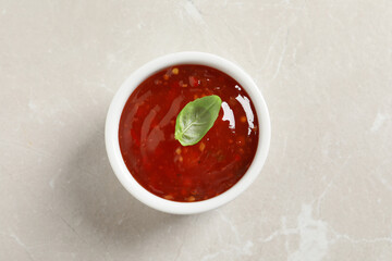 Spicy chili sauce with basil on light table, top view