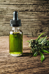 Glass bottle with herbal organic medicine CBD concentrate, droplet dosing a biological and ecological hemp plant herbal pharmaceutical cbd oil from a jar and medical cannabis bud on wooden background