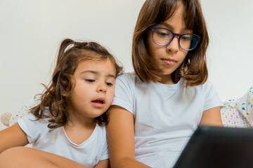 Two girls sitting on their beds with a tablet.