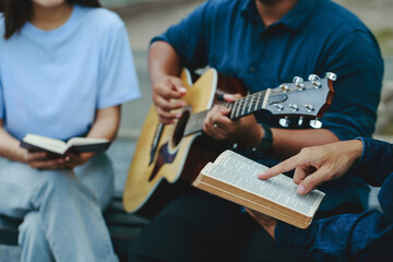 Christian families worship God in the garden by playing guitar and holding a holy bible. Group Christianity people reading the bible together.Concept of wisdom, religion, reading, imagination.