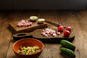 Salad in a clay plate on a table on a wooden table next to chopped vegetables and sausage on the planks.