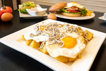 Typical Spanish tapa of broken eggs with eels to share on a restaurant table with other dishes in the background