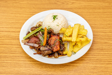 Stylish presentation of a traditional Peruvian recipe for sautéed tenderloin with vegetables, a garnish of homemade potatoes and a bowl of overturned white rice