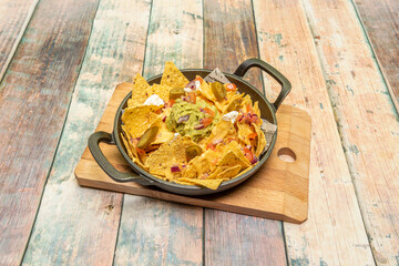 Cast iron pie pan with serving of Mexican corn nachos with guacamole, chopped red onion, sliced...