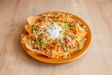 Plate of nachos with guacamole, beans and baked melted cheese on wooden table