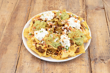 Overflowing plate of Mexican corn nachos with guacamole, cream cheese, chopped white onion, julienne tomato, chili con carne and jalapenos