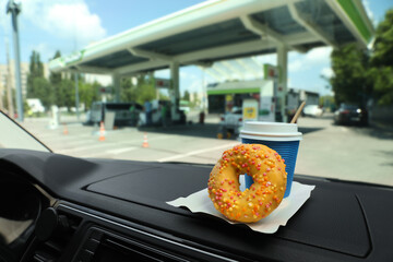 Paper coffee cup and doughnut on car dashboard at gas station