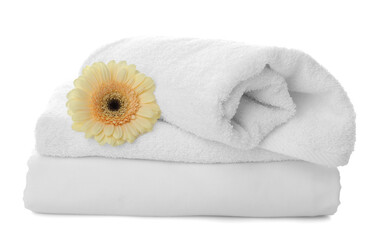 Fototapeta na wymiar Fresh clean towels, bed sheet and gerbera on white background