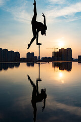 Silhouette of flexible acrobat doing handstand on the dramatic sunset and cityscape background. Concept of individuality, creativity and outstanding
